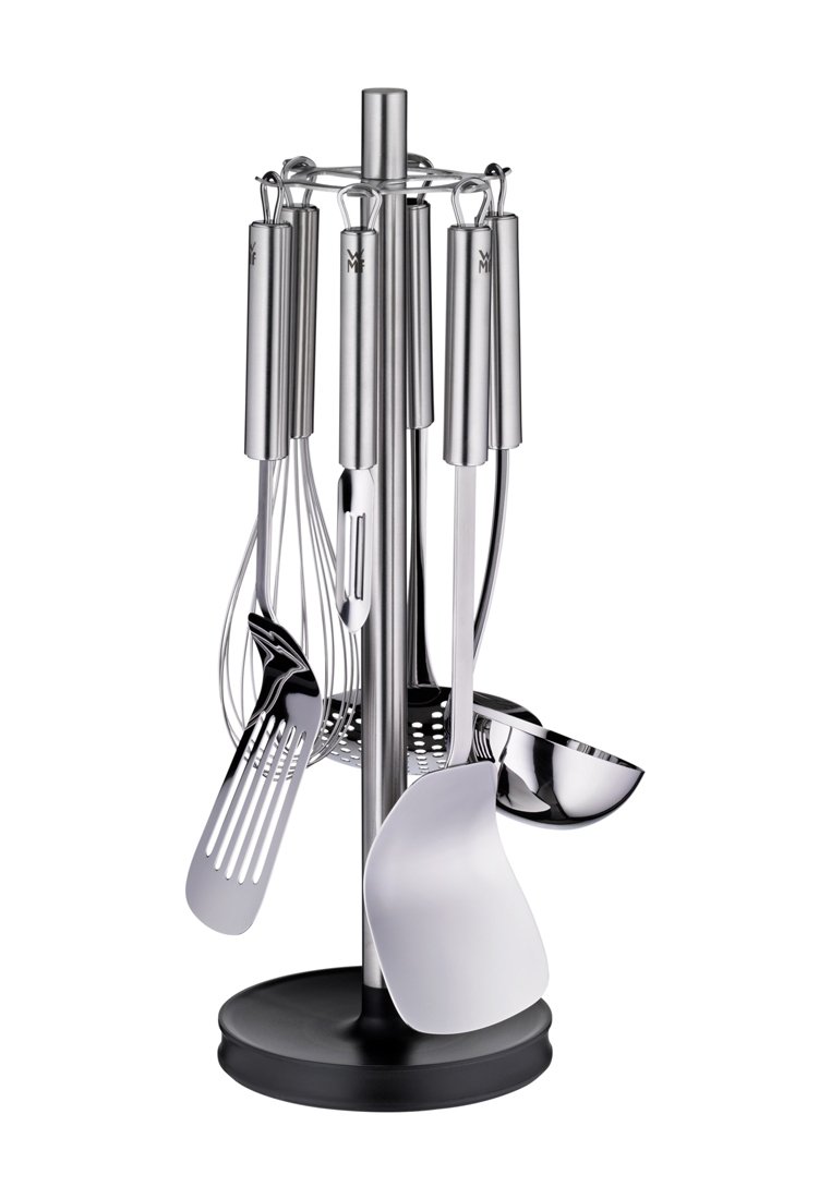 Ensemble d'ustensiles en acier inoxydable sur une base noire, comprenant un fouet, une spatule à fentes, une louche et une cuillère, fixés à un support vertical.