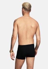 Svarta bomullsboxer med en mjuk midja, med en åtsittande design och slät yta. Synliga tatueringar på överarmarna.