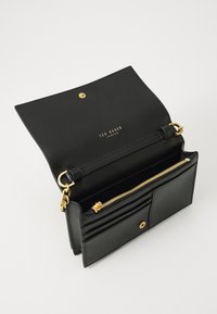 Bolsa de mão de couro preto com detalhes em dourado, apresentando um compartimento com fecho e slots para cartões. Logotipo embutido na aba interna.