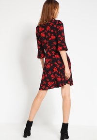 Czarna sukienka w kwiaty z czerwonymi kwiatami, rozkloszowanymi rękawami i dopasowaną talią. Kończy się nad kolanem. Połączona z czarnymi botkami za kostkę.
