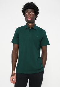 Polo de cor verde escuro feito de tecido texturizado, com colarinho de três botões e um discreto bordado de logótipo no lado esquerdo do peito.