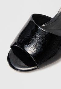 Melnas atvērtā pirksta slaida sandales ar spīdīgu, strukturētu virsmu un gludu, noapaļotu zoli. Siksna, kas pārklāj augšējo pēdas daļu, ir plata.