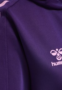 Paarse sportieve hoodie gemaakt van gladde stof, met een lichtroze logo en contrasterende stiksels.