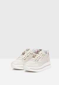 Sneaker in pelle beige con suola bianca spessa, dotate di occhielli metallici e lacci decorati con gemme rosa. Accenti rosa sul tallone.