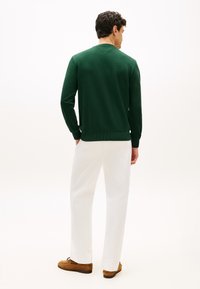 Πράσινο φούτερ με ριμπ μανσέτες και τελείωμα, σε συνδυασμό με λευκό παντελόνι και καφέ σουέντ παπούτσια. Η πίσω όψη παρουσιάζει ελάχιστες λεπτομέρειες.