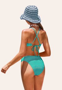 Bikini de cuadro vichy verde y blanco con tirantes cruzados y lazo en la espalda. Combinado con un sombrero de cubo azul texturizado y collar de conchas.