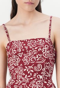 Burgundy klänning med vit blommönster, med tunna axelremmar och en åtsittande bodice. Lätt bomullstyg med en mjuk textur.