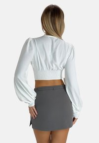 Witte cropped top met pofmouwen en een gesmockte achterkant, gecombineerd met een aansluitende grijze minirok met een subtiel taile-detail.