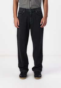Black denim jeans with a relaxed fit, featuring front pockets, copper rivets, and a simple design. Worn with black sneakers.