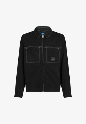 Czarna kurtka z długim rękawem, z zamkiem błyskawicznym z przodu, dwiema kieszeniami na piersi, białym kontrastowym przeszyciem oraz małą czarną łatą z logo na prawej kieszeni.