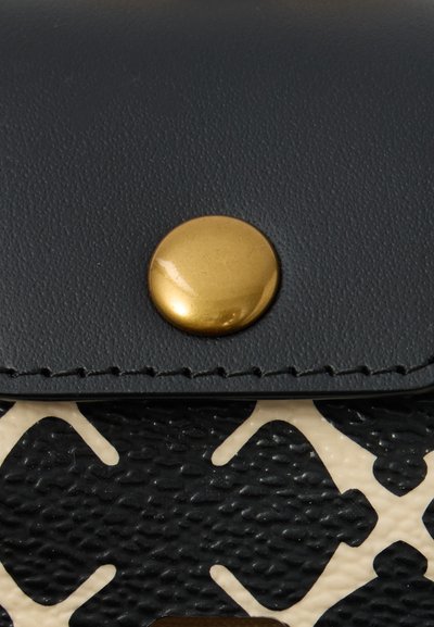 Prim-plan al unui capac de portofel texturat negru cu un buton circular auriu și o parte dintr-o suprafață cu un model alb-negru dedesubt.