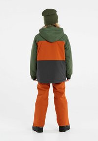 Farbblockierte Jacke in Grün, Orange und Grau, kombiniert mit orangenen Hosen. Verfügt über eine Kapuze und elastische Bündchen, mit einer strukturierten Oberfläche.