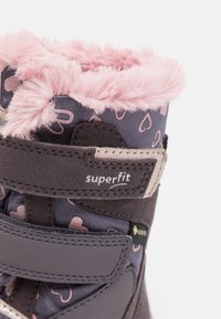 Violetiniai sniego batai su rožine kailio apdaila, širdelių raštu ir Velcro dirželiais. Šone yra logotipas „superfit“ ir vandeniui nepralaidi membrana.