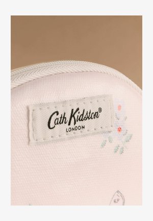 Prim-plan al unui material alb cu textură țesută vizibilă, având o etichetă cusută Cath Kidston London și un model floral mic în culori delicate.