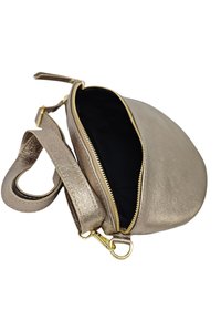 Sac en bandoulière doré métallique avec une forme incurvée, fermeture éclair et intérieur noir ; il dispose d'une longue sangle et d'une texture lisse.