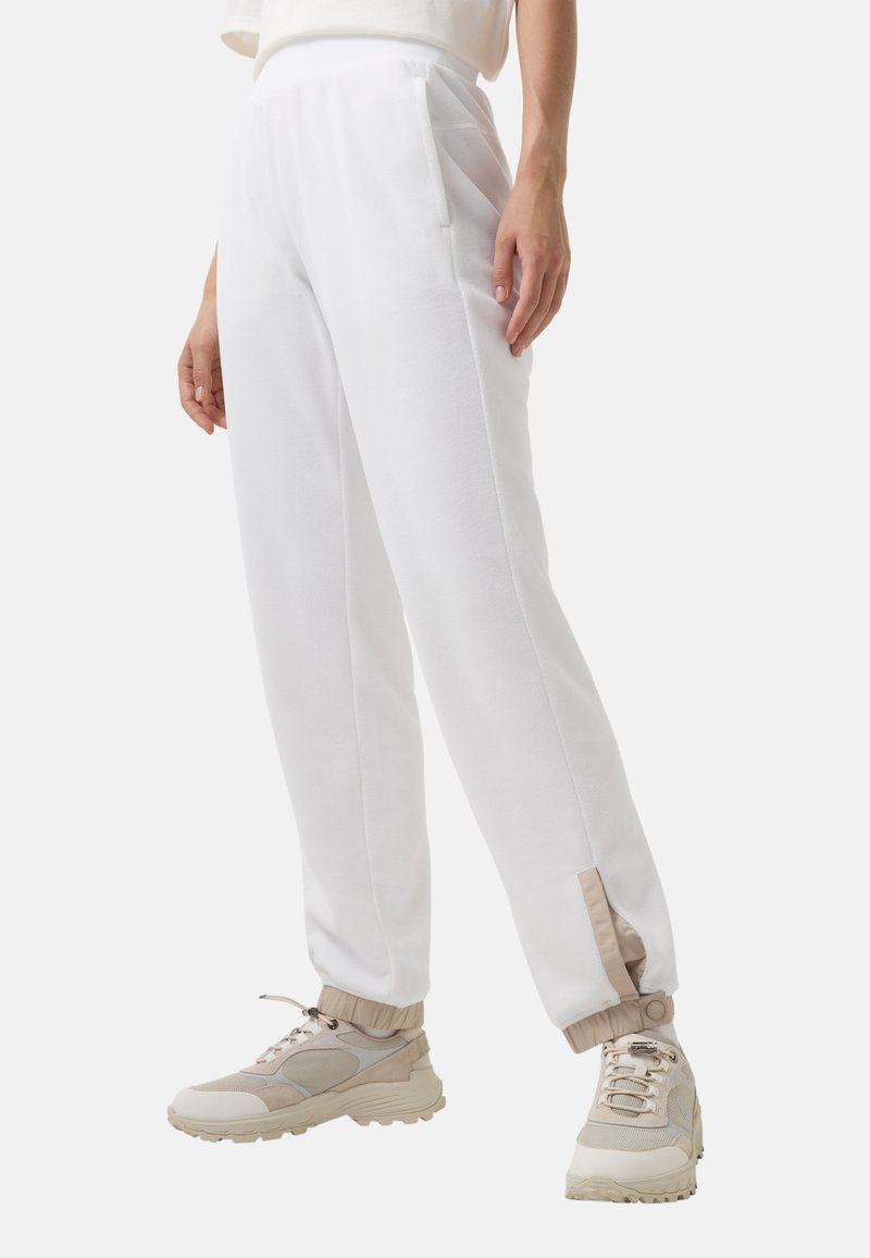 Hvide fleece sweatpants med sidelommer, tapered manchetter med en kontrasterende beige detalje, parret med beige træningssko.