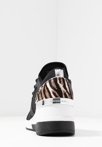 Černá teniska s leopardím potiskem, strukturovanou textilií, lesklými stříbrnými doplňky, tlustou bílou podrážkou a hladkým černým špičkovým zakončením.