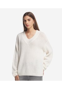 Hvid strikket sweater med V-udskæring, oversized pasform og ribbede manchetter. Tekstureret stof med løs vævning, der giver et afslappet look.