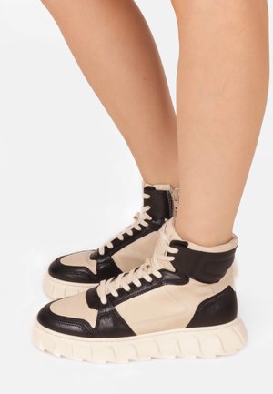 Sneaker alte con una combinazione di colori crema e nero, realizzate in materiali in pelle e sintetici, collo imbottito e suola spessa e testurizzata.