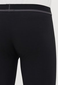 Svarta tights med en slät yta, med en bred elastisk midja i grått. Sömdetaljer löper längs sidorna. Designade för komfort.