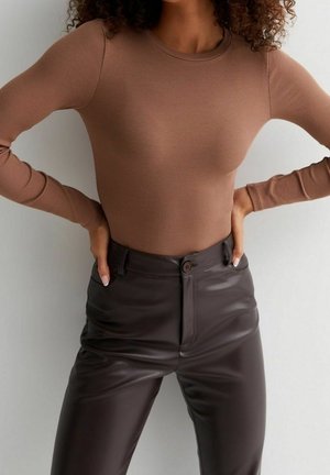 Top lungo a maniche lunghe marrone a costine abbinato a pantaloni in finta pelle lucida marrone scuro a vita alta, caratterizzati da chiusura con bottone e tasche frontali.