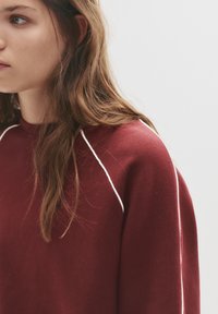 Bordeaux sweatshirt met een ronde hals, featuring witte accentstiksels langs de schouders. Zachte textuur, normale pasvorm, minimalistisch ontwerp.