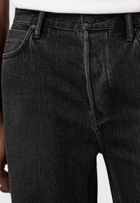 Jean en denim noir à coupe slim, doté d'un design classique à cinq poches, fermeture à bouton métallique et coutures contrastantes.