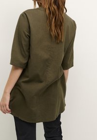 Olivegrünes Leinen-Tunika mit kurzen Ärmeln und abgerundetem Saum, leichte Textur, leicht lockere Passform und minimalistischem Design.