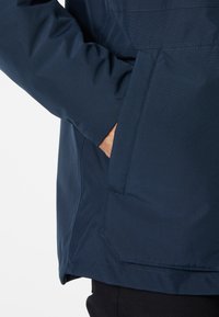 Chaqueta azul, ligera y de textura suave, con un bolsillo lateral y costuras limpias a lo largo del dobladillo y las mangas.