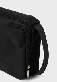 Sac en tissu noir de forme rectangulaire, doté d'une fermeture éclair, d'une poignée latérale et d'une surface texturée.