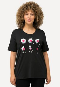 Camiseta negra de algodón con un estampado gráfico de margaritas blancas con centros rosas y corazones. Manga corta, escote redondo, ajuste casual.