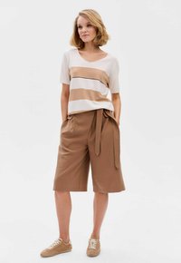 Tan en crèmekleurig gestreept T-shirt met korte mouwen en V-hals, gecombineerd met bruine high-waisted shorts met een strikriem. Compleet met beige sneakers.
