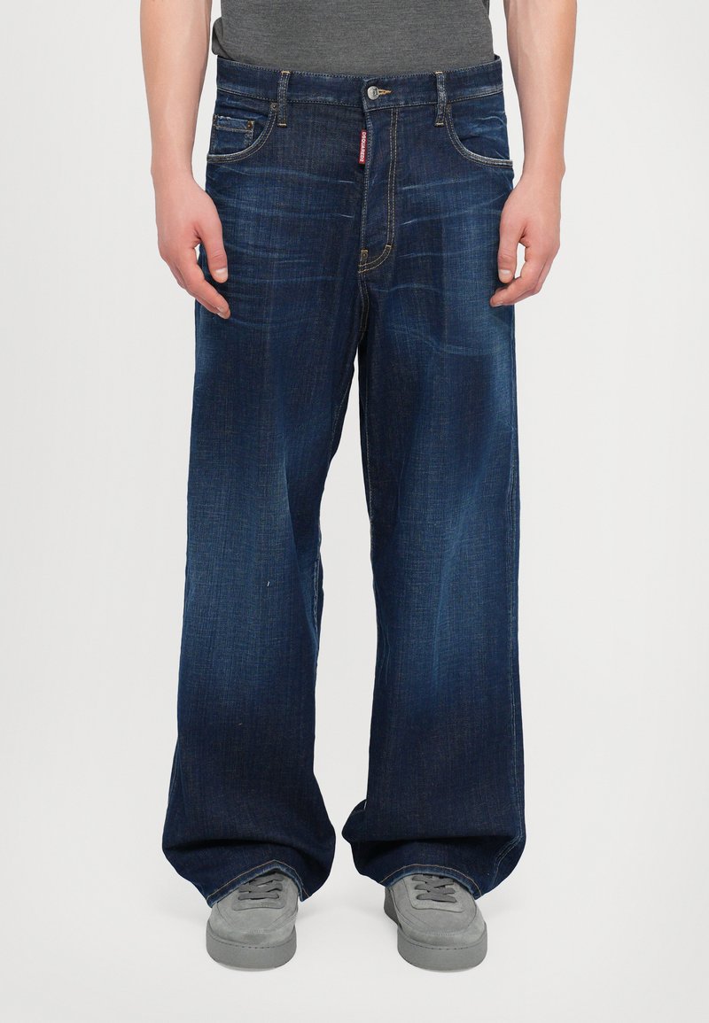 Jean en denim bleu foncé, coupe ample avec jambes droites. Comprend cinq poches, un léger effet délavé et des garnitures en argent au niveau de la taille.