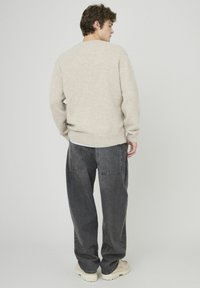 Pull beige en maille avec une coupe décontractée, manches longues et ourlet côtelé. Porté avec un jean ample gris foncé et des chaussures de couleur claire.
