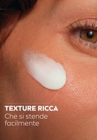 Crema bianca sulla pelle, texture liscia, facilmente spalmabile; primo piano della pelle con una tonalità marrone chiaro, pori fini visibili.