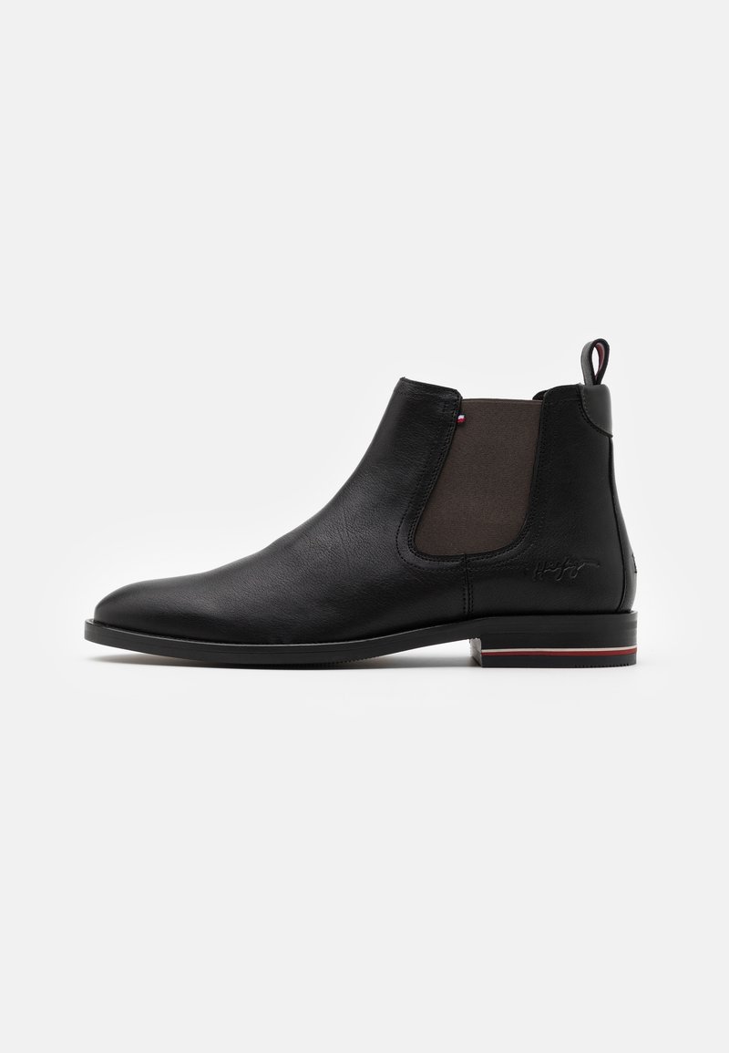 Botte Chelsea en cuir noir avec panneau latéral élastique, petit talon avec rayures rouge et blanc, et languette de traction à l'arrière sur fond blanc.