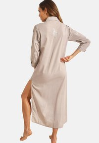 Robe longue grise avec un col et des manches trois-quarts, présentant une broderie florale blanche sur les manches et le dos, avec des fentes sur les côtés.