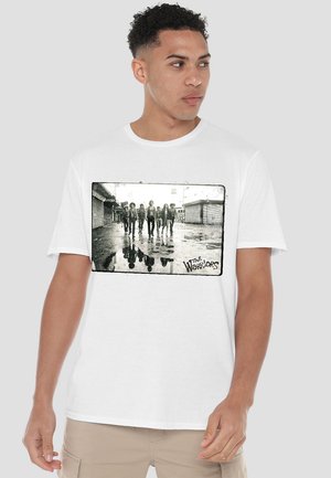 White cotton t-shirt featuring a black-and-white graphic print of a gang walking on a wet street, with "The Warriors" text in the corner.