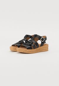 Sandales en cuir noir avec plusieurs brides, boucle réglable et semelle en liège. Texture lisse et design ouvert à l'avant.