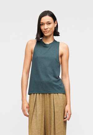 Haut sans manches couleur sarcelle en tissu doux avec un col rond, associé à un pantalon plissé marron clair. Coupe simple et décontractée.