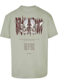 Light green cotton t-shirt featuring a large graphic of two doves and stylized text "BIRD OF PEACE" in maroon. Text includes a quote below.