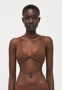Brun bikini topp med et teksturert mønster, dyp scoop halslinje og brede stropper, med et vridd sentrumdesign.