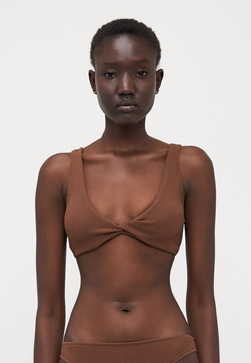 Brun bikini topp med et teksturert mønster, dyp scoop halslinje og brede stropper, med et vridd sentrumdesign.