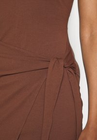 Robe marron avec un détail de côté noué, faite à partir d'un tissu doux et texturé. Silhouette lisse et ajustée avec une ligne de couture discrète.