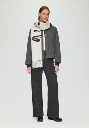 Grijze textuur jas met een cropped ontwerp, gecombineerd met zwarte wijde jeans en een witte sjaal met een zwart lippenafdruk en franjes.