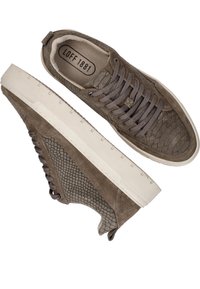 Bruine suède sneakers met textuurpanelen aan de zijkant, platte veters en een witte rubberen buitenzool. Logo zichtbaar aan de binnenkant.