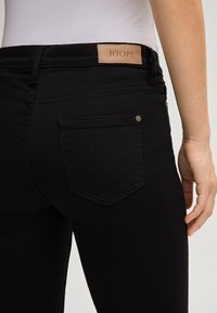 Zwarte denim jeans met een gladde textuur, voorzien van een leren taillebandlabel "JOOP!" en een klassiek achterzakontwerp met stikselaccenten.