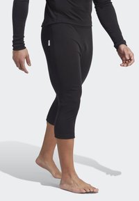 Black fitted leggings made of smooth fabric, cropped just below the knee, featuring a small brand tag on the side.