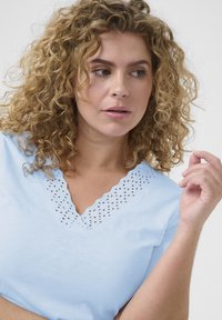 Camiseta de cuello en V de color azul claro, hecha de suave algodón, con detalles de encaje de ojal en el escote y las mangas cortas.