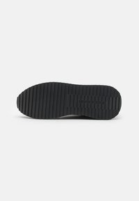 Suola nera di sneaker con profonde scanalature orizzontali per aderenza. Realizzata in gomma, presenta una forma arrotondata e un design minimalista.